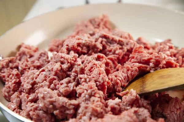 Close up of a wooden spoon in raw ground beef in a frying pan