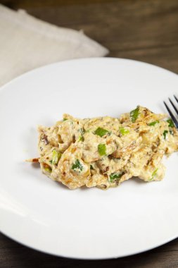 Krem peynirle hazırlanmış tatlı karides ve yeşil soğan beyaz bir tabakta, ahşap bir masanın üzerinde bronz bir peçetenin yanında.