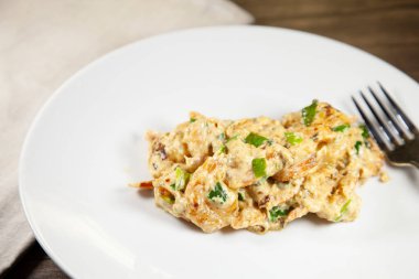 Krem peynirle hazırlanmış tatlı karides ve yeşil soğan beyaz bir tabakta, ahşap bir masanın üzerinde bronz bir peçetenin yanında.