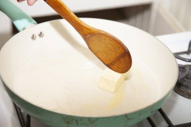 Tahta bir kaşıkla eriyen tavaya tereyağı sürüyorum.