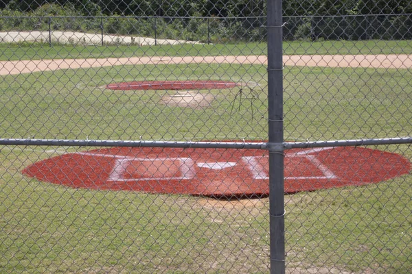 Home plate of an empty baseball field through a fence