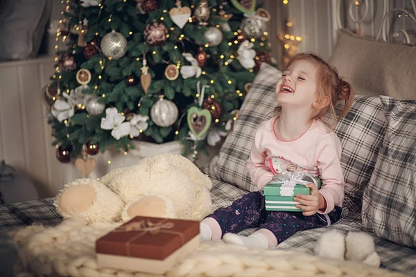 Merry Christmas and Happy Holidays! Little beautiful girl with her presents sits in her bed. Gifts for your daughter at Christmas. Christmas holiday concept