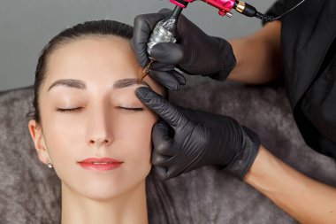 Genç bir kız için kalıcı makyaj prosedürü. Güzel bir kadın, pürüzsüz, genç bir cilt, bir güzellik uzmanında oturuyor. Bir güzellik uzmanı kalıcı kaş modelliği yapar. Kalıcı makyaj tedavisi..
