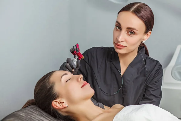 Permanent make up procedure, applying on young girl. Beautiful woman with smooth, young skin, sitting in a beautician. A beautician performs modeling permanent eyebrows makings.Permanent makeup treatment.