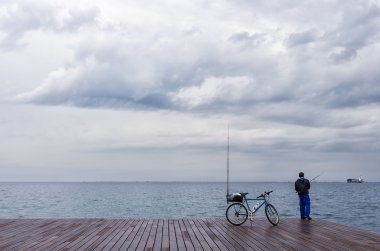12 Mart 2016-Selanik, Yunanistan, deniz kıyısında bir bisiklet ile Fisherman, bulutlu bir gökyüzü altında