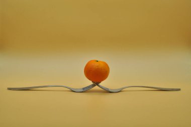 Nötr turuncu arkaplan üzerine izole edilmiş iki iç içe geçmiş çatal üzerinde dengelenmiş mandalina.