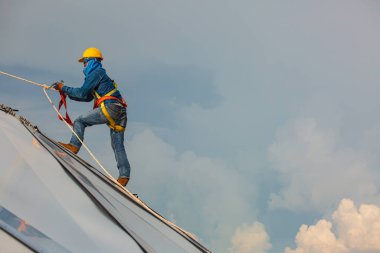 Erkek işçiler halat ile yükseklik güvenliğine bağlanıyor, emniyet kemerine bağlanıyor, çatıya bağlanıyor, düşüş tutuklaması ve düşme demirleme noktası sistemleri yükselmeye hazır, inşaat alanı petrol tankı kubbesi