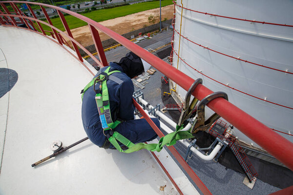 Male worker wearing safety first harness and safety lone working at high handrail place on open top tank roof oil