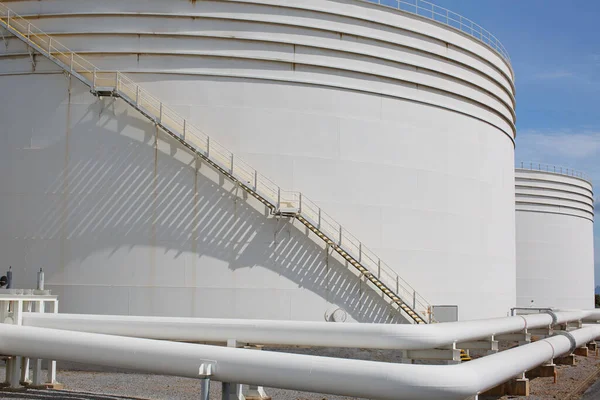 Large Industrial tanks for oil with a walkway up and down of oil storage tank metal stairs on the side of an industrial oil container.