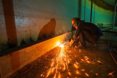Erkek işçi metali tank alt çelik plaka üzerinde kıvılcımlar kesiyor. Yakın çekim ışığı parlıyor. Koruyucu eldiven takıyor ve kapalı alanda maske takıyor..