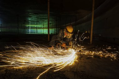 Erkek işçi metali tank alt çelik plaka üzerinde kıvılcımlar kesiyor. Yakın çekim ışığı parlıyor. Koruyucu eldiven takıyor ve kapalı alanda maske takıyor..
