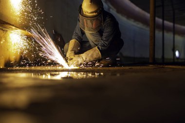 Erkek işçi metali tank alt çelik plaka üzerinde kıvılcımlar kesiyor. Yakın çekim ışığı parlıyor. Koruyucu eldiven takıyor ve kapalı alanda maske takıyor..