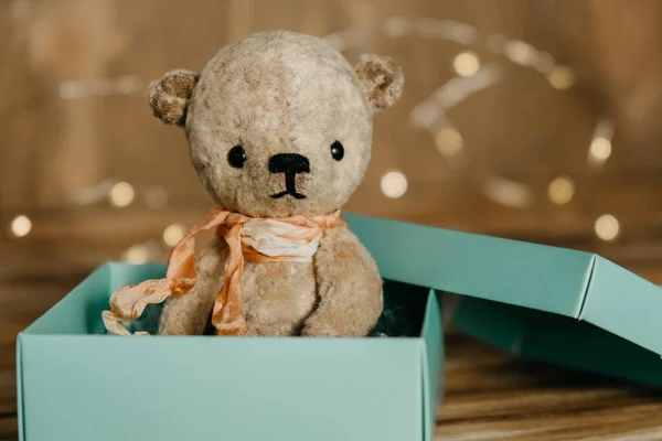 Sitting teddy bear in a gift box on a blurred wooden background. Gifts and surprises for any occasion. Selective focus. Copy space.