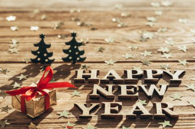 Mesajlı Noel kartı, afiş, mutlu yıllar. Konfeti, mektuplar, küçük köknar ağaçları, parlak ışıklandırılmış ahşap arka planda bir hediye. Seçici odak.