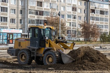 RUSSIA, ANGARSK - 17 Ekim 2020 İnşaat, şehrin yerleşim alanındaki bir yolun onarımı. Yol yapımında kullanılan makineler yol boyunca ezilmiş taşlar dağıtıyor..