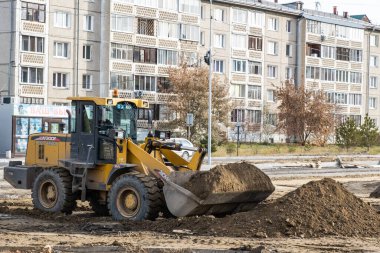 RUSSIA, ANGARSK - 17 Ekim 2020 İnşaat, şehrin yerleşim alanındaki bir yolun onarımı. Yol yapımında kullanılan makineler yol boyunca ezilmiş taşlar dağıtıyor..