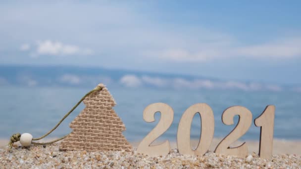 Numéros en bois 2021 et une décoration d'arbre de Noël se tiennent sur le sable à la plage. Concept de tourisme, de loisirs et de voyages. — Video