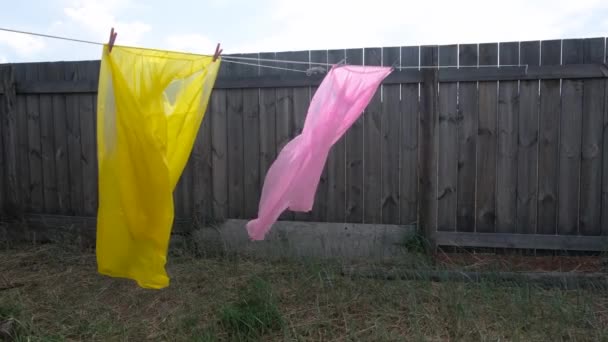 フェンスの背景に家の中庭の風から2つのレインコートピンクと黄色のフラッタ. — ストック動画