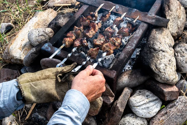 Delicious appetizing grilled meat, cooked on a fire in the courtyard of a country house. Mens hands turn them over. — Stok fotoğraf