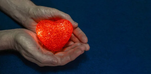 Corazón rojo brillante en manos masculinas sobre un fondo azul oscuro. Concepto de San Valentín. Primer plano. Copiar espacio. — Foto de Stock