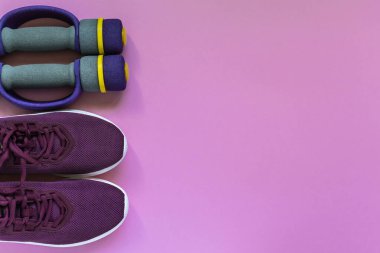 Spor ayakkabıları ve halterler evde ve spor salonunda, pembe arka planda. Vücut bakımı konsepti, aktif yaşam tarzı. Üst Manzara. Metin için boşluk.