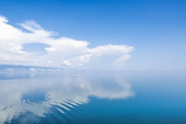 Suyun sakin yüzeyine güzel bir bulut yansıyor. Uzakta bir tekne hareket ediyor. Açık bir gün ve günaydın hava. Boşluğu kopyala.