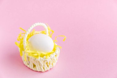 Beyaz Paskalya yumurtası pembe arka planda küçük bir hasır sepetin içinde. Bayram afişi tebrik kartı. Seçici odaklanma. Boşluğu kopyala.