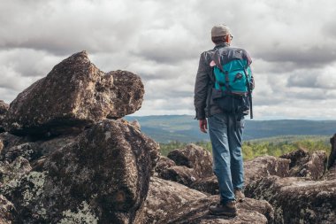 Sırt çantalı bir turist dağın tepesinde duruyor ve yukarıdan manzaranın tadını çıkarıyor. Spor ve aktif yaşam kavramı.