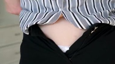 Orta yaşlı bir kadın kilo aldıktan sonra dar siyah pantolonları iliklemeye çalışıyor. Obezite problemleri. Diyet kavramı.