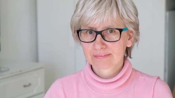 Hermosa mujer adulta amistosa de mediana edad que usa gafas sonríe y endereza su cabello, en el interior. De cerca.. — Vídeos de Stock