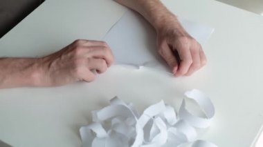 Sinirli, hasta bir insanın ellerini yakın plan çekerek kağıdı yavaşça parçalara ayırıp bir kenara fırlatan birinin..