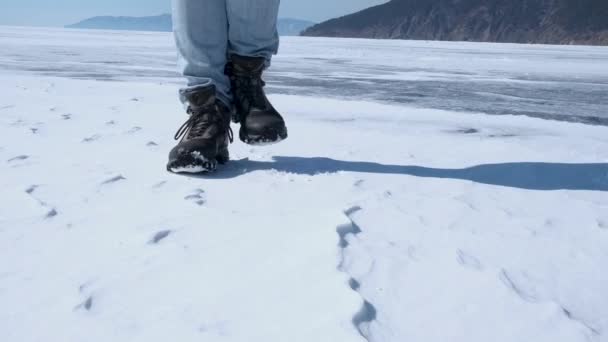Nohy muže v trekingových botách poskakují a dupou ve sněhu. Detailní záběr. — Stock video