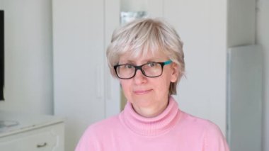 Güzel, orta yaşlı, gözlüklü, gülümseyen ve kameraya bakan bir kadın. Yüz portresini yakından çek.