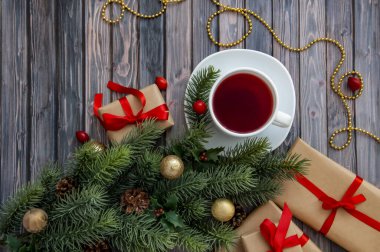 Noel ağacının dalları, koniler, kırmızı böğürtlenler, hediyeler ve ahşap bir masada bir fincan çay. Noel dekoru.