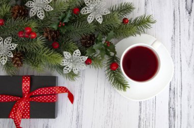 Noel ağacının dalları, koniler, kırmızı böğürtlenler, hediyeler ve ahşap bir masada bir fincan çay. Noel dekoru.