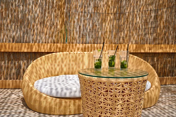 Yaz tatilinde sahilde. Hasır kanepe ve içki ve kokteyllerle dolu bir masa.