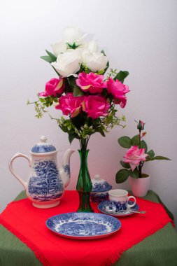 Bir fincan kahve, kahve makinesi, çaydanlık, şeker kasesi ve pembe çiçekli vazo ile kahvaltı servisi..