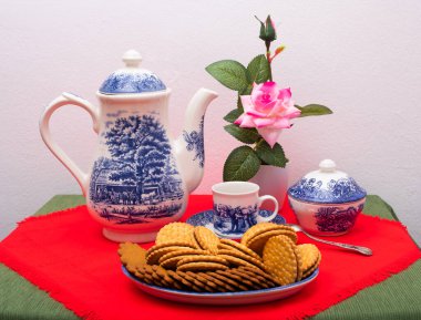 Çikolatalı kurabiye, bir fincan kahve, kahve makinesi, çaydanlık ve pembe çiçekli vazo..