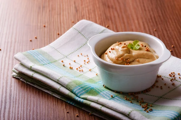 Bowl with mustard and seeds on green cloth and wooden board — Stock Photo, Image