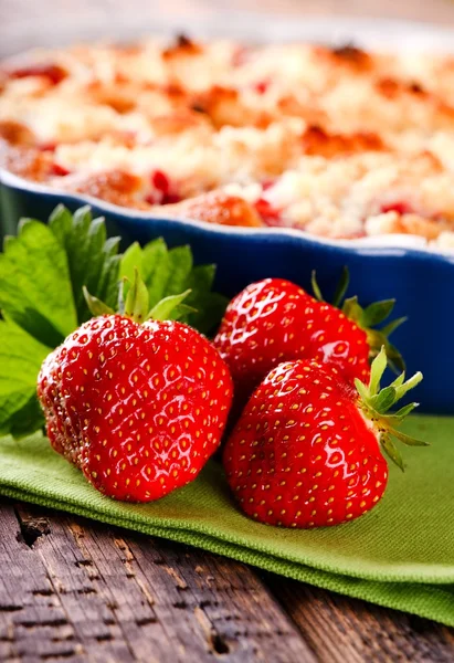 Three fresh red strawberries in front of fruit cake on green towel — Stock Photo, Image