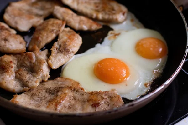 Жареные яйца и куриное мясо на сковороде — стоковое фото