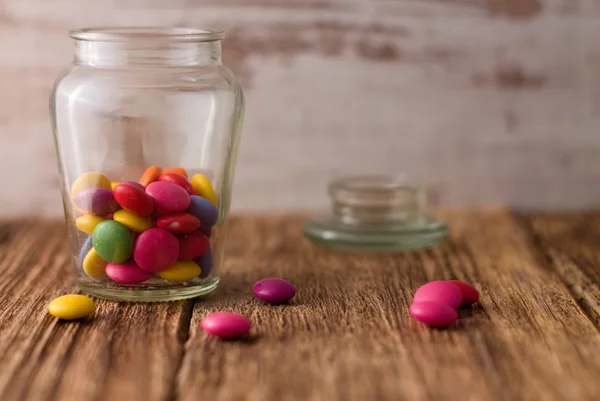 Farbe Schokolade Smarties im Glas und herum auf Holzbrett — Stockfoto