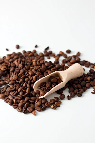 Куча зерна кофе на белой доске с деревянной ложкой — стоковое фото