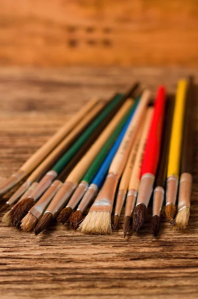 Color paintbrushes on vertical photo placed on wooden board — Stock Photo, Image