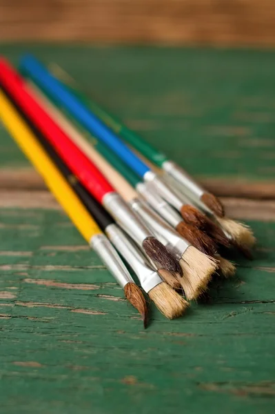 Paintbrushes placed on green worn wooden board — Stock Photo, Image