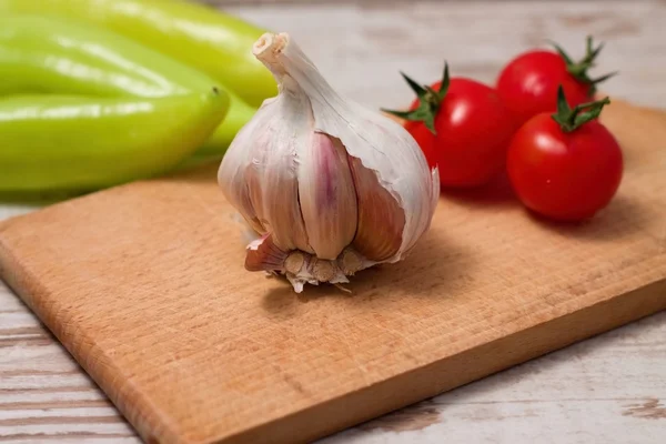Single garlic bud on chopping board with tomatoes