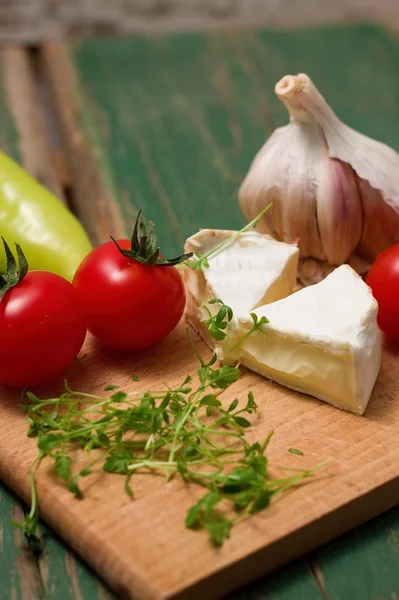 Dos rebanadas de camembert y verduras en la tabla de cortar — Foto de Stock