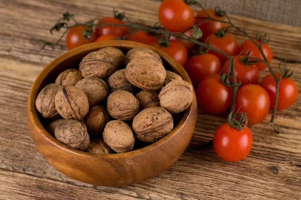 Bowl full of walnuts and branch with tomatoes — Stock Photo, Image