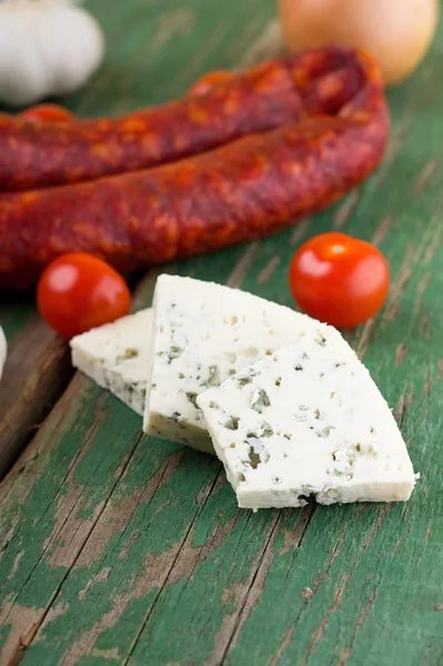 Three slices of danish blue cheese in front of spicy sausages — Stock Photo, Image