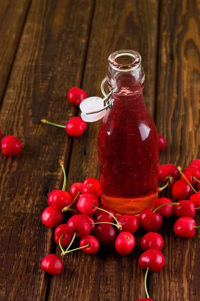Красный вишневый напиток в бутылке посреди фруктов — стоковое фото
